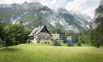 A large building amidst a green meadow with mountains in the background. The landscape is picturesque and inviting.