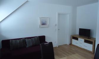 A modern living room with a dark red sofa and a television. The room is bright and friendly with a simple table and a picture on the wall.