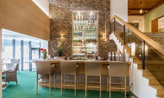 An elegant bar with modern stools and a decorative shelf full of drinks. The area is brightly lit and offers an inviting atmosphere.