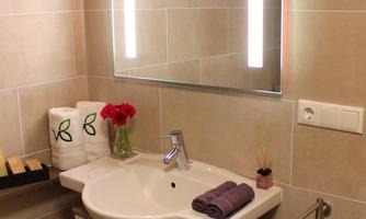 A modern bathroom with a sink, a mirror, and elegant lighting. On the shelf, there are towels and a flower vase.