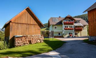 A picturesque country house with flower boxes and a woodpile in the foreground. Surrounded by green meadows and a clear sky.