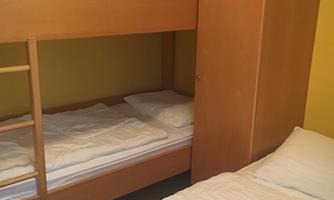 A simple room with a wooden bunk bed and a single bed. The walls are painted in a light yellow.