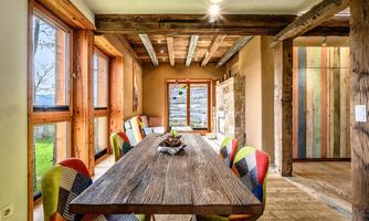 A stylish dining room with a large wooden table and colorful chairs. Large windows let in plenty of light and offer a view of the outdoors.
