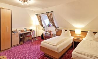 A cozy hotel room with two single beds and a seating area. The room is bright and friendly, with a purple carpet and a desk.
