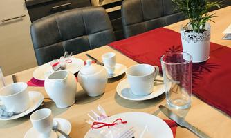 A beautifully set table with dishes, glasses, and a small plant. The red tablecloth adds a cozy atmosphere to the modern kitchen.