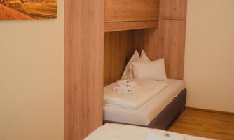 A simple room with two beds and a wooden piece of furniture that provides a sleeping place. A picture of a mountain landscape hangs on the wall.