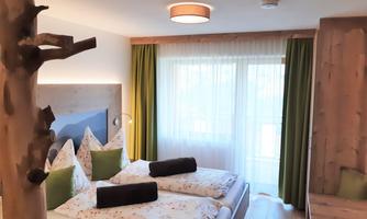 A cozy bedroom with two single beds and a bright, friendly atmosphere. Large windows with curtains provide plenty of daylight.