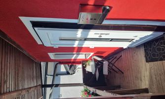 A narrow balcony with a red wall and a white door. There is a small table and two chairs, perfect for relaxing.