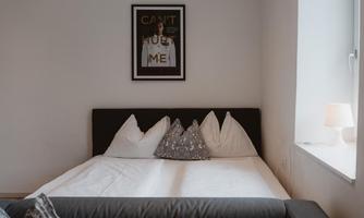 A cozy bedroom with a large bed and decorative pillows. A striking picture hangs on the wall with the text "CAN'T HURT ME".