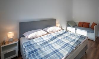 A modern bedroom with a large bed and a checkered blanket. Pleasant lighting and a cozy seating area complement the space.