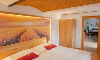 A cozy bedroom with a wooden bed and red pillows. The wall is decorated with a beautiful picture of a golden field.