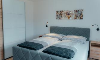 A modern bedroom with a comfortable double bed and stylish bedside lamps. The walls are light and adorned with decorative wall art.