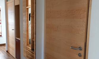 A bright hallway with wooden flooring and a wooden interior door. There is a mirror on the wall and cabinets are built in.