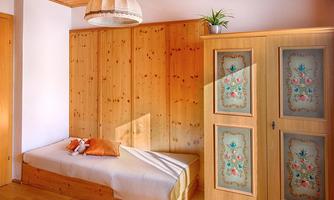 A cozy bedroom with wood paneling and a daybed. The room is bright and has a decorative wardrobe front with a floral design.