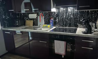 A modern kitchen with dark cabinets and a marbled wall. It is equipped with a sink, cooktop, and various kitchen appliances.