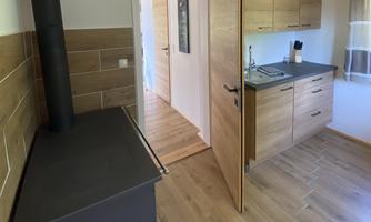 A modern kitchen with wooden cabinets and a wood stove. The floor is made of light wood and the space feels bright and inviting.
