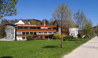 A modern hotel with the inscription "Friends of Nature" stands in front of a green meadow. In the background, there are trees and a blue sky.