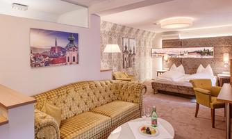 An elegant hotel room with a comfortable sofa and a large bed. On the table, there is a drink and a small snack.