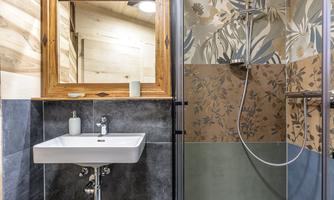 A modern bathroom with a sink and a shower stall. The walls are adorned with decorative tiles and a mirror.