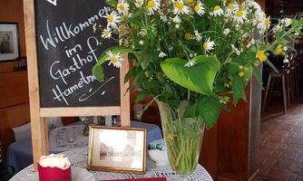 A welcome sign in the inn with fresh flowers in a vase.  
On the table lies a red book and a candle.
