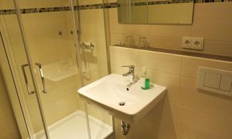 A modern bathroom with a shower and sink. The walls are tiled in light colors and the furnishings are simple and functional.