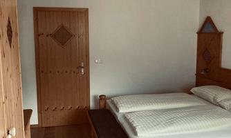 A cozy bedroom with wooden beds and a rustic wardrobe. The walls are bright, and the ceiling has exposed beams.