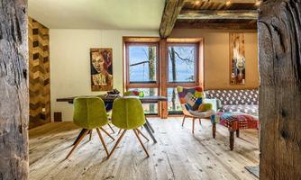 A modern living room with wooden floors and large windows. The furnishings consist of colorful furniture and artworks on the walls.