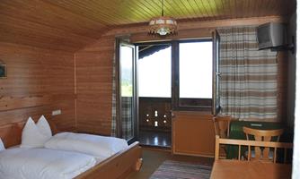 A cozy room with wood paneling, a double bed, and a table. Large windows provide a view of nature.