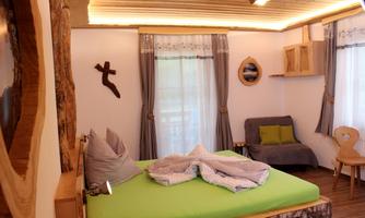 A cozy bedroom with a large bed and green bedding. There are natural wood details and large windows that let in plenty of light.