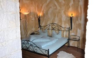 A cozy bedroom with an elegant iron bed and soft lighting. The walls are painted in warm tones, creating an inviting atmosphere.