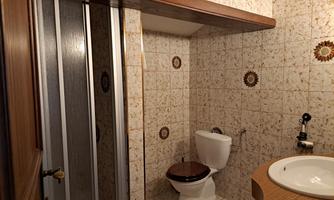 A small bathroom with a shower, a toilet, and a sink. The walls are adorned with decorative tiles.