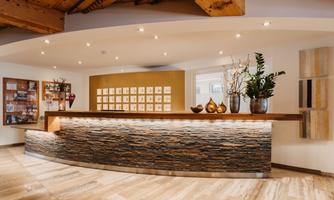 A modern reception area with an elegant, curved stone counter. The decor is stylish and decorated with plants, creating an inviting atmosphere.
