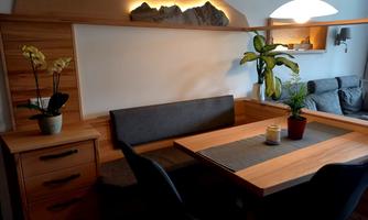 A cozy dining area with wood paneling and a bench. There are plants and a candle on the table.