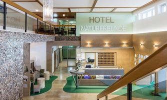 A modern hotel lobby with a reception desk and stylish seating areas. The walls are in calm colors, and large windows provide plenty of daylight.
