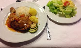 A plate with fried chicken, rice, potatoes, and vegetables. Next to it, a fresh salad with green leafy vegetables and tomatoes.