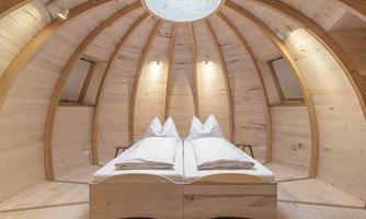 A modern, wood-clad room with a double bed and a round skylight. The walls are designed with light wood, creating a cozy atmosphere.