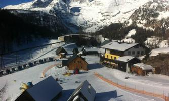 A snowy landscape with pretty cottages and majestic mountains in the background. The sun is shining and the sky is clear.