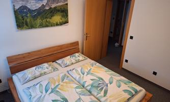 A cozy bedroom with a wide bed and colorful bedcovers. A landscape painting with mountains and forests hangs on the wall.