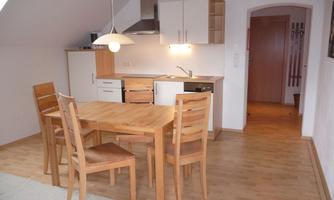A modern dining room with a wooden table and four chairs. The kitchen is open and well-equipped.