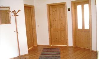 A bright hallway with wooden doors and a wooden coat rack. The floor is covered with a colorful carpet.