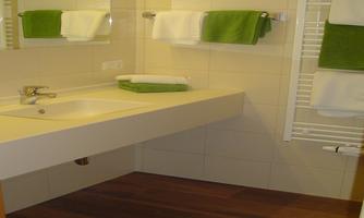 A modern bathroom with a sink and a large mirror. Green towels add a fresh touch to the space.