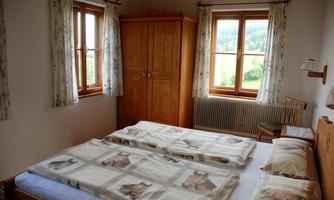 A cozy bedroom with two beds and bright wood interiors. Large windows provide a view of the green landscape outside.