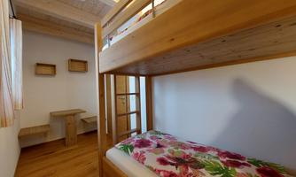 A cozy room with a wooden bunk bed. The colorful bedding and the simply furnished structure give the space an inviting atmosphere.