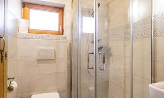 A modern bathroom with a glass shower and a toilet. Bright tiles and a wooden ceiling create a friendly atmosphere.