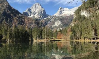 A clear lake surrounded by majestic mountains and green trees. The surface of the water reflects the landscape.