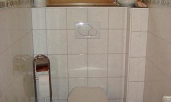 A small bathroom with a toilet, a sink, and a window. The walls are tiled, and there is a towel rack.