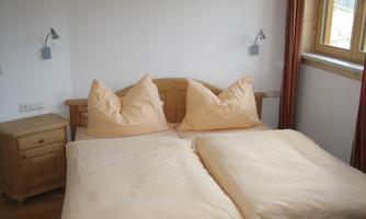 A cozy bedroom with a double bed and pillows shaped like hills. On the wall are practical reading lamps and a bedside table made of wood.