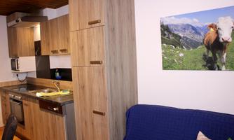 A modern kitchen with wooden furniture and a refrigerator. On the wall hangs a picture of a cow in a green landscape.