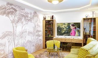 A modern living room with yellow armchairs and a sofa. On the wall, there is a TV showing a girl with a backpack.