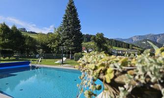 A beautiful pool with clear water, surrounded by trees and mountains. The sky is blue and the landscape is green.